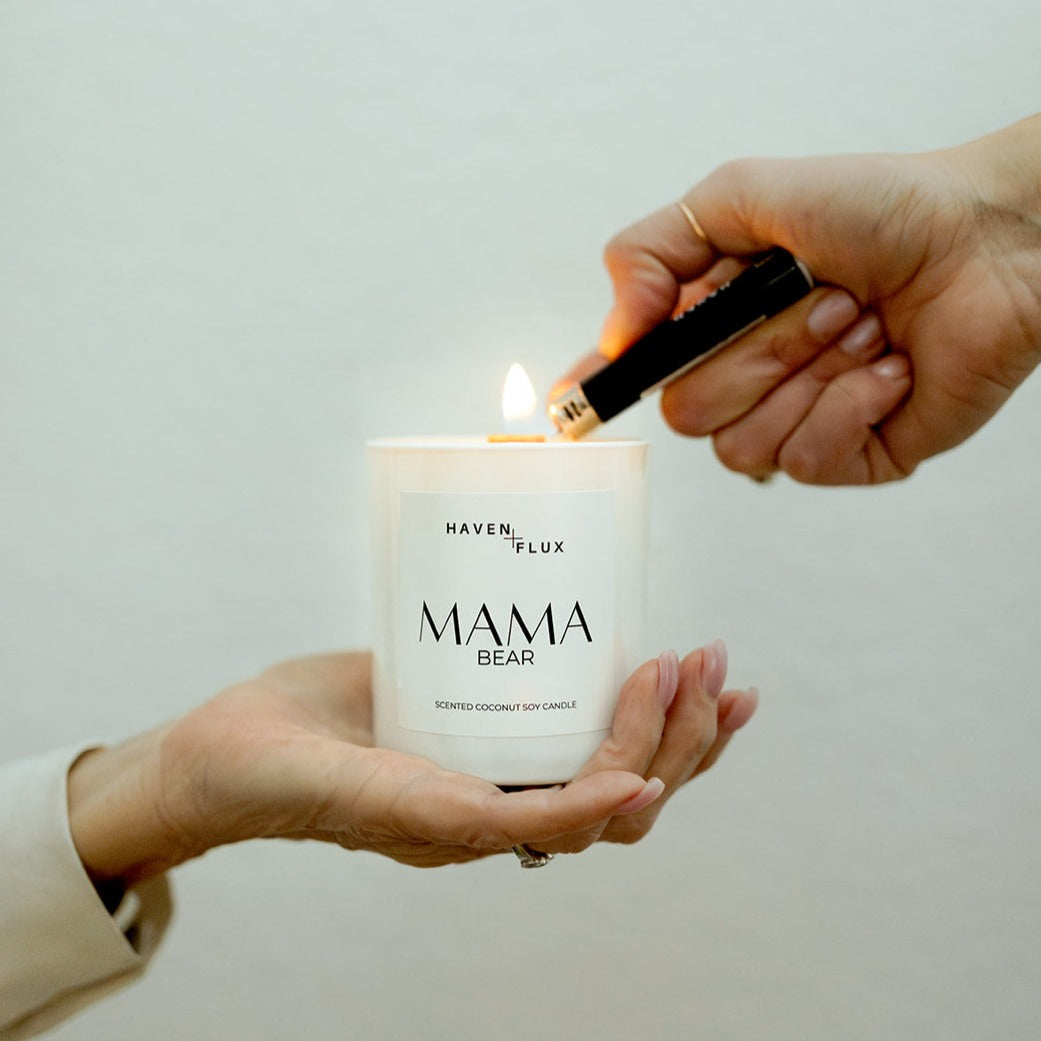 A mother holding the Mama Bear Wooden Wick Candle while her daughter lights it. The candle is formulated with luxury, non-toxic ingredients and features scent notes of wild flowers, fresh lavender, and mountain air, creating a serene and bonding moment between mother and daughter.